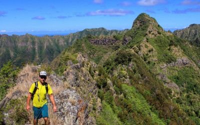 Hiker on a green mountain ridge trail on O'ahu